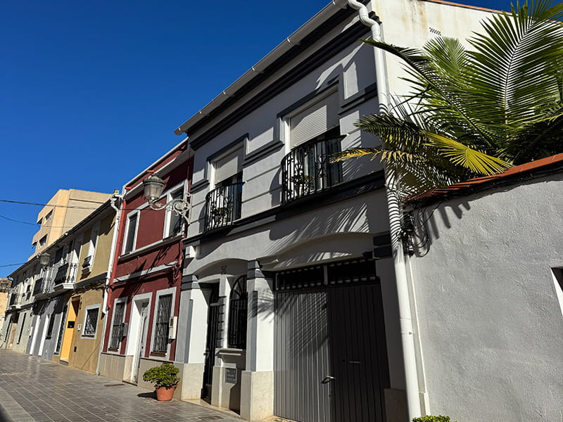 Невысокие дома с балконами и пальмой на тихой улице района Poblados del Oeste (Валенсия). How-To Spain