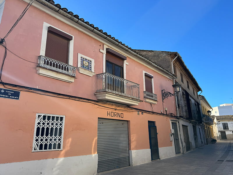Розовый дом с балконами и вывеской «Horno» на улице района Poblados del Oeste (Валенсия). How-To Spain