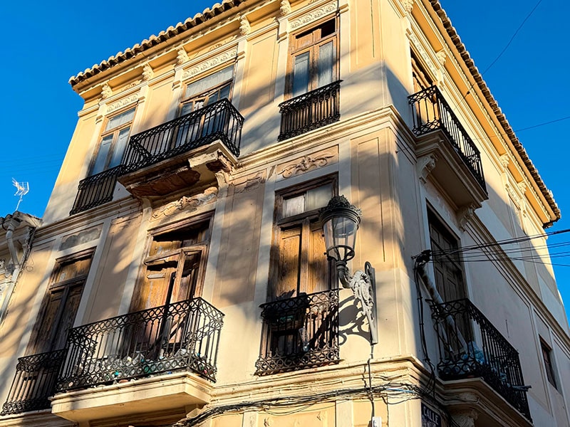 Крупный план фасада старинного углового дома с коваными балконами и уличным фонарём в районе Кабаньял (Валенсия).
