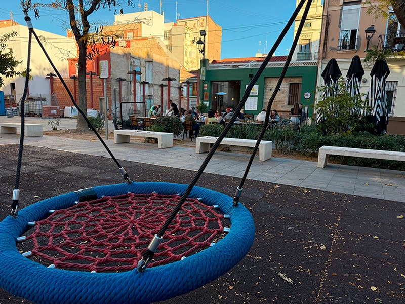 Большие круговые качели на детской площадке; на заднем плане &mdash; терраса бара и лавочки в районе Кабаньял (Валенсия).