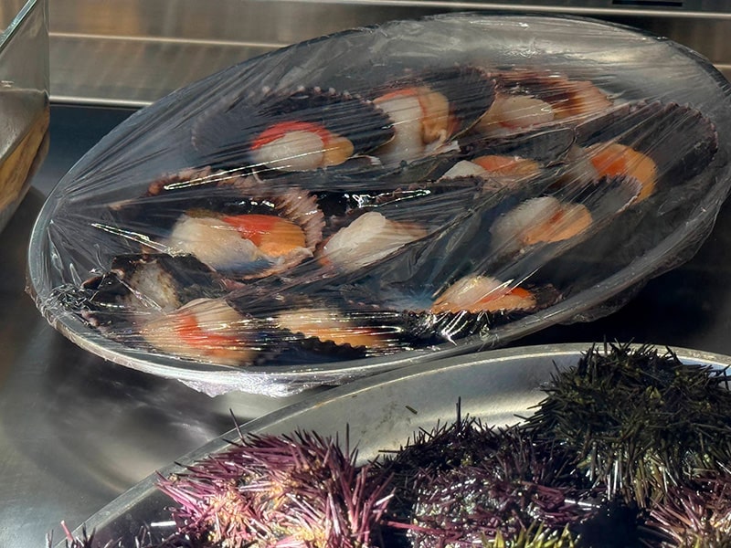 Тарелка с морепродуктами под плёнкой на витрине; на переднем плане &mdash; морские ежи (Кабаньял, Валенсия).
