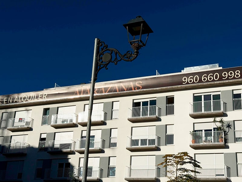 Уличный фонарь на фоне белого дома с балконами и вывеской Atarazanas в районе Кабаньял (Валенсия).