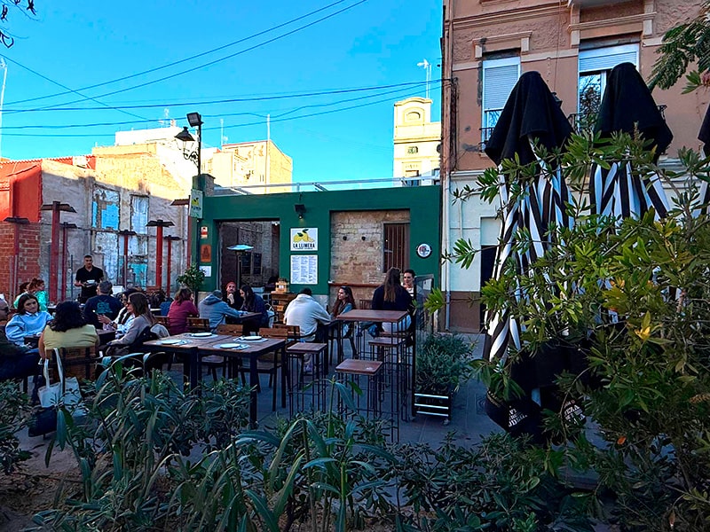 Терраса уличного бара с посетителями, столами и зонтиками во дворе в районе Кабаньял (Валенсия).