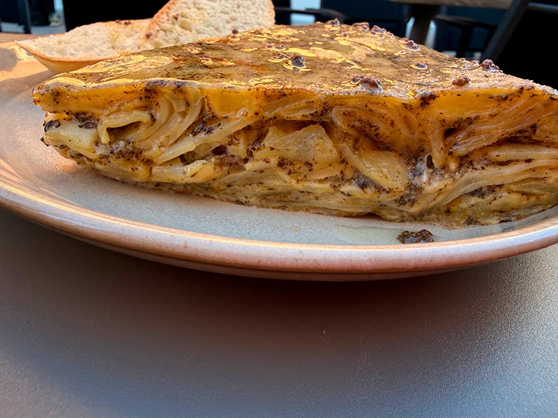 Кусок испанской тортильи с картофелем на тарелке; на заднем плане &mdash; ломтики хлеба (Кабаньял, Валенсия).