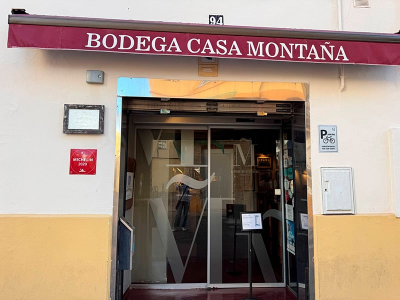 Вход в Bodega Casa Monta&ntilde;a под бордовой маркизой с вывеской и табличкой Michelin на фасаде в районе Кабаньял (Валенсия).