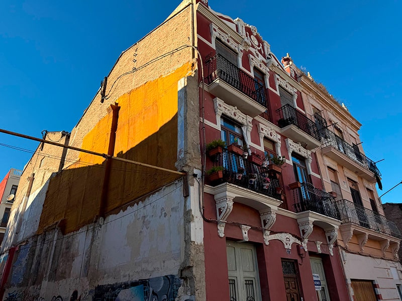 Фасад старинного розового дома с декоративной лепниной и балконами на углу улицы в районе Кабаньял (Валенсия).