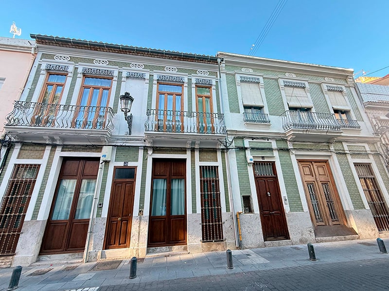 Традиционный фасад домов в Кабаньяле с зелёной плиткой, деревянными дверями и балконами с коваными ограждениями (Валенсия).