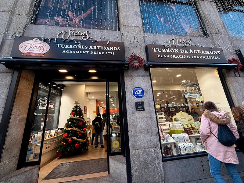 Фасад магазина Vicens Turrones Artesanos в центре Мадрида с рождественской витриной и наряженной елкой у входа