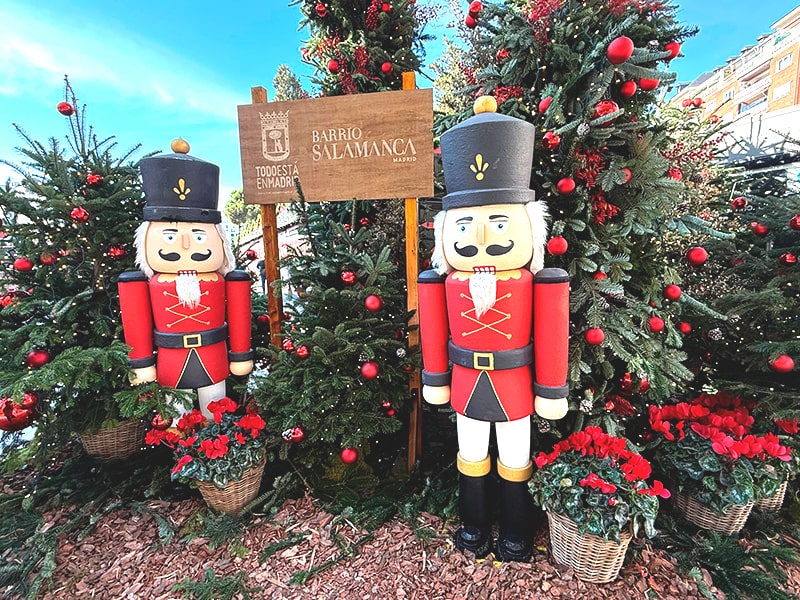 Рождественский декор в Barrio Salamanca в Мадриде: две фигуры Щелкунчиков среди елей с красными шарами и табличкой района