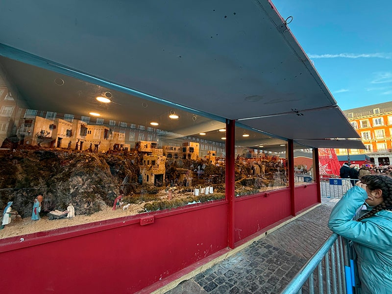 Большой рождественский вертеп в стеклянной витрине на Plaza Mayor в Мадриде, люди смотрят на сцену через ограждение