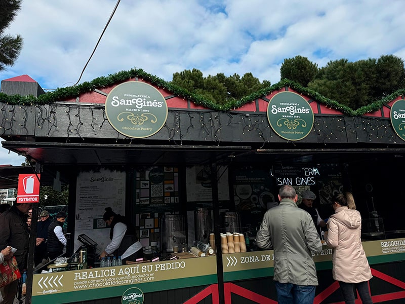 Рождественний киоск Chocolatería San Ginés на Plaza de Colón в Мадриде: посетители заказывают чуррос и горячий шоколад у стойки.