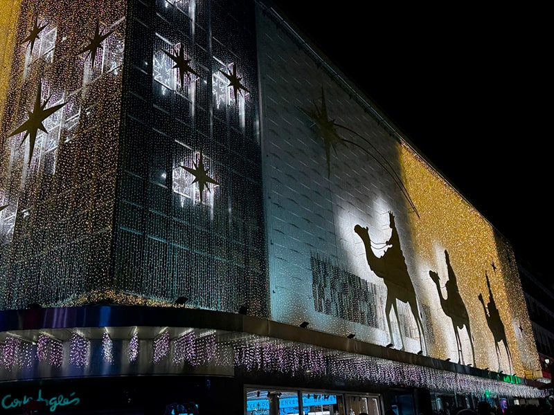Рождественская иллюминация на фасаде El Corte Inglés в районе Preciados–Callao в Мадриде, золотые огни и силуэты Трех королей на верблюдах на ночном небе