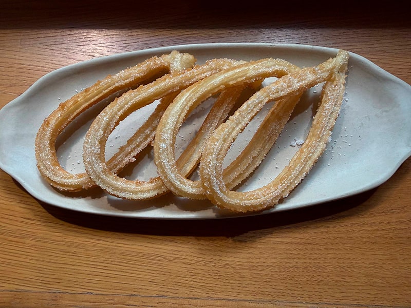 Тарелка классических испанских чуррос, посыпанных сахаром, на деревянном столе