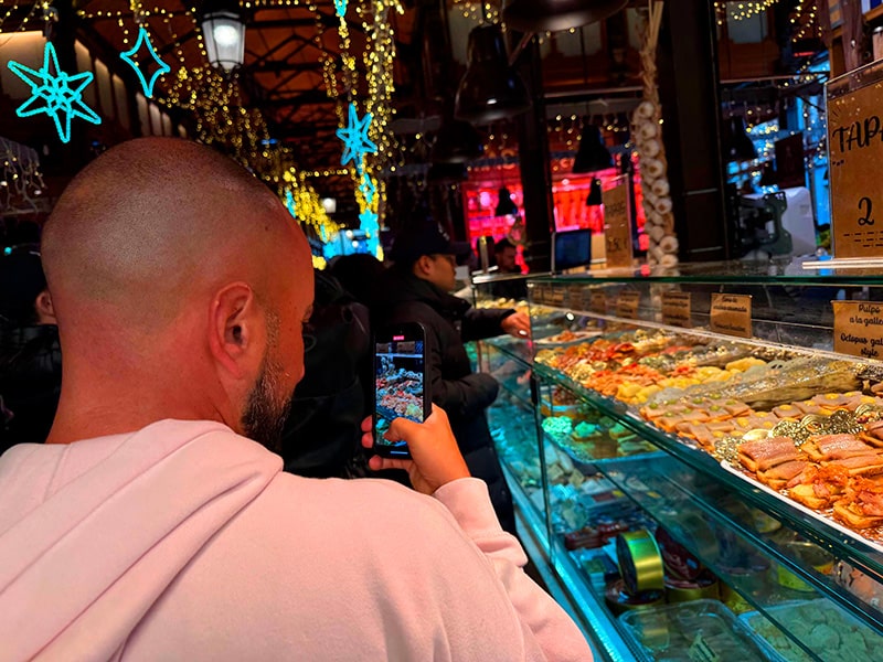 Посетитель фотографирует витрину с тапас и морепродуктами на рождественски украшенном рынке San Miguel в Мадриде