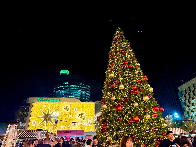 Большая рождественская ёлка на Mercado de Navidad у El Corte Inglés Castellana в Мадриде, на заднем плане световой фасад с золотой звездой и ангелами