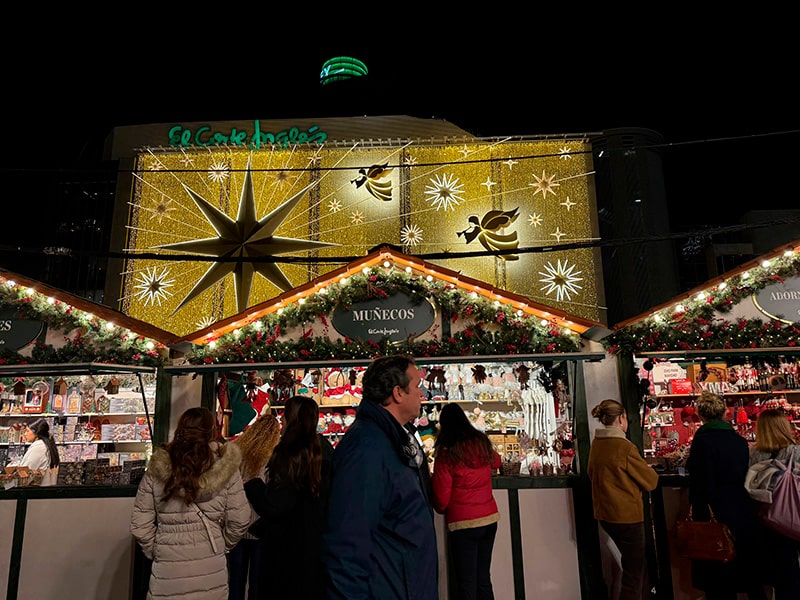 Рождественские домики Mercado de Navidad у El Corte Inglés Castellana в Мадриде на фоне световой фасадной инсталляции с большой звездой и ангелами
