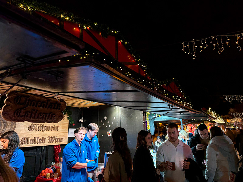 Люди у рождественского уличного киоска с горячим шоколадом и глинтвейном, украшенного огоньками ночью