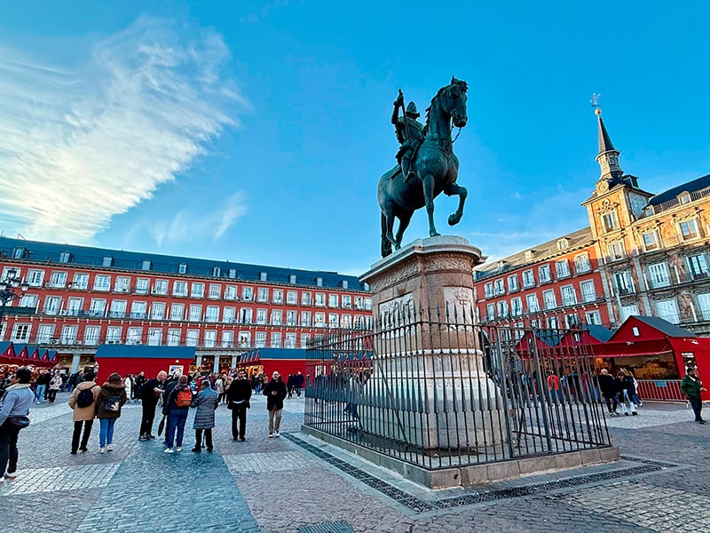 Площадь Plaza Mayor в Мадриде с конной статуей Филиппа III и рождественскими красными павильонами рынка