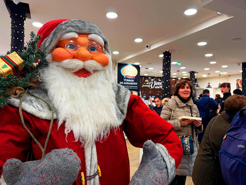 Фигура Санта-Клауса в магазине Vicenç Turrones Artesanos на фоне очереди покупателей за рождественским турроном