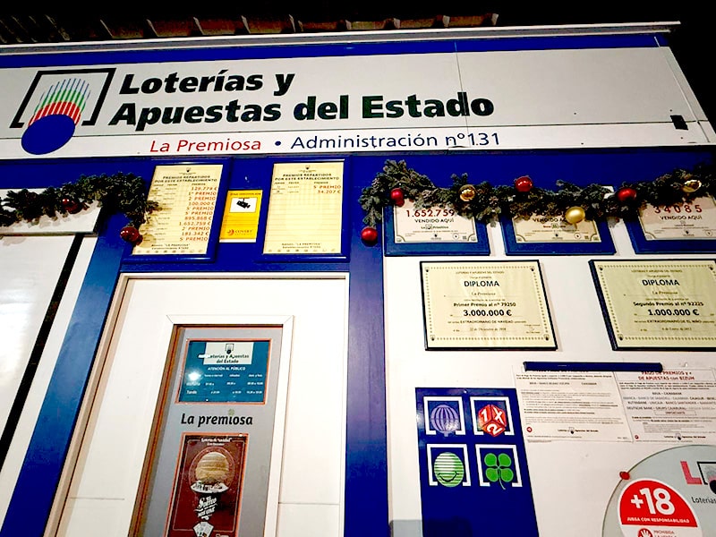Лотерейная администрация La Premiosa №131 в Испании с вывеской Loterías y Apuestas del Estado, дипломами о крупных выигрышах и рождественским декором над окнами