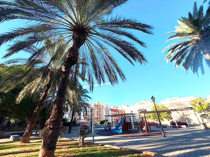 Пальмы и детская площадка на солнечной площади в квартале Cabanyal района Poblados Mar&iacute;timos в Валенсии