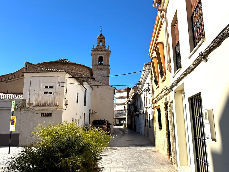 Узкая улица с традиционными домами и колокольней церкви в посёлке Benim&agrave;met района Poblados del Oeste в Валенсии