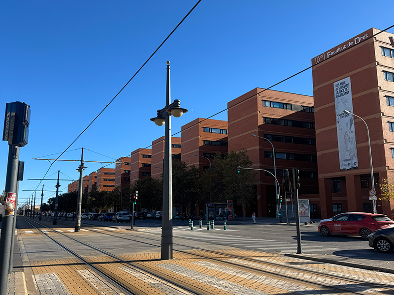 Трамвайные пути и остановка рядом с кампусом Universitat de València в районе Algirós: кирпичные корпуса факультетов вдоль проспекта, ясное небо и городское движение.