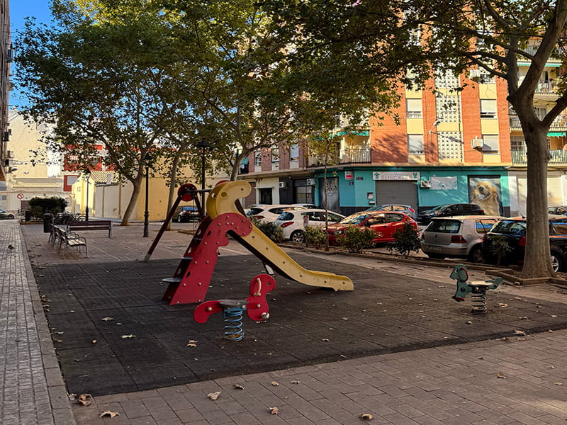 Alt: Детская площадка с горкой и качалками под деревьями во дворе жилого квартала в районе Беникалап, Валенсия, Испания