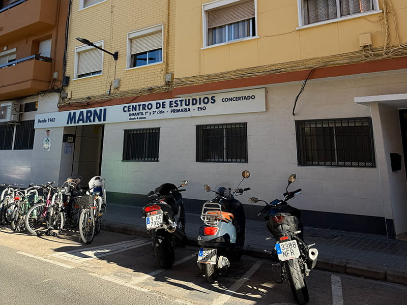 Фасад школы Marni Centro de Estudios в Валенсии: вывеска учебного центра и припаркованные велосипеды и мотоциклы у входа