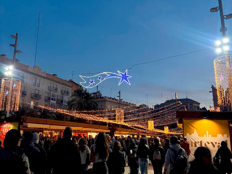 Вечерний рождественский рынок на Plaza de la Reina в Валенсии под гирляндами и световой кометой