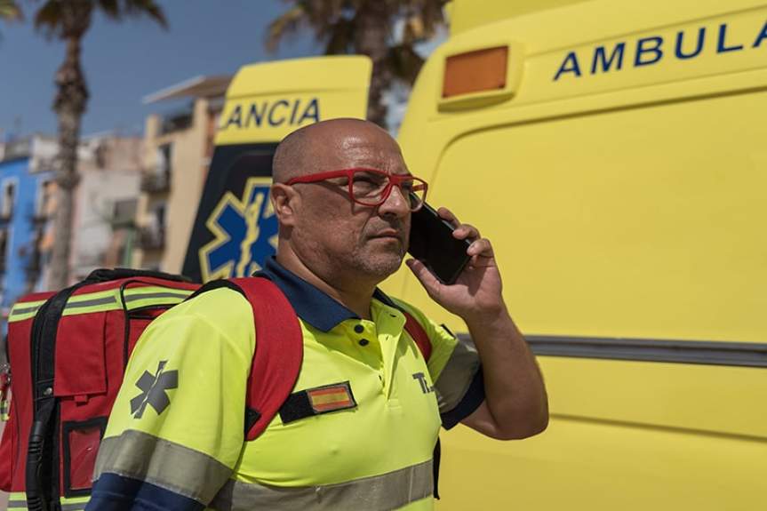 Испанский медик разговаривает по телефону на фоне машины скорой помощи