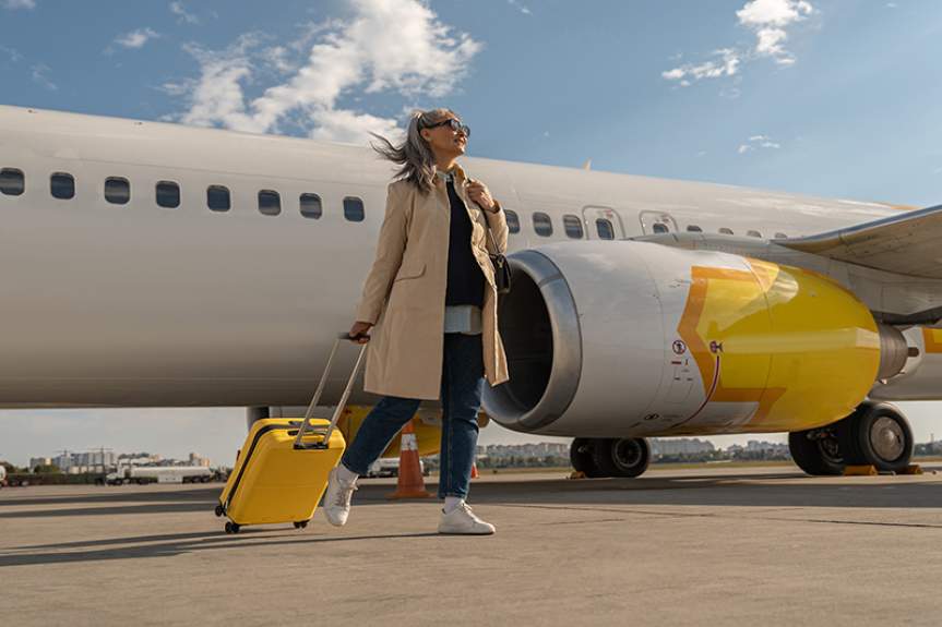 Женщина с чемоданом на фоне самолета в аэропорту